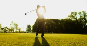 Golfer swinging a club on a sunny course, illustrating how Pilates can enhance your golf game.