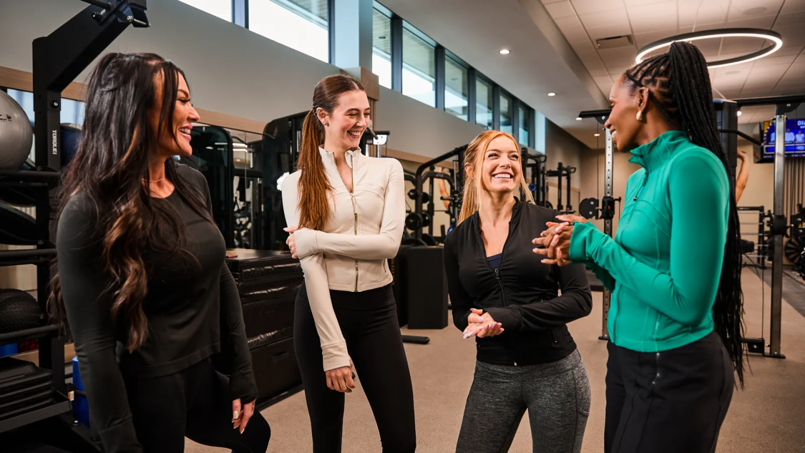 Group of women in activewear at a gym, discussing how to start running together.
