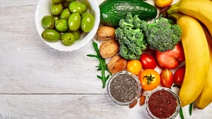 Assorted liver healthy foods including olives, avocado, broccoli, nuts, bananas, and chia seeds on a wooden table.