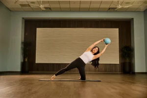 Woman practicing hot pilates with a ball in a studio, showcasing the NEW CLASS FORMAT: HOT PILATES MOVATI Athletic.