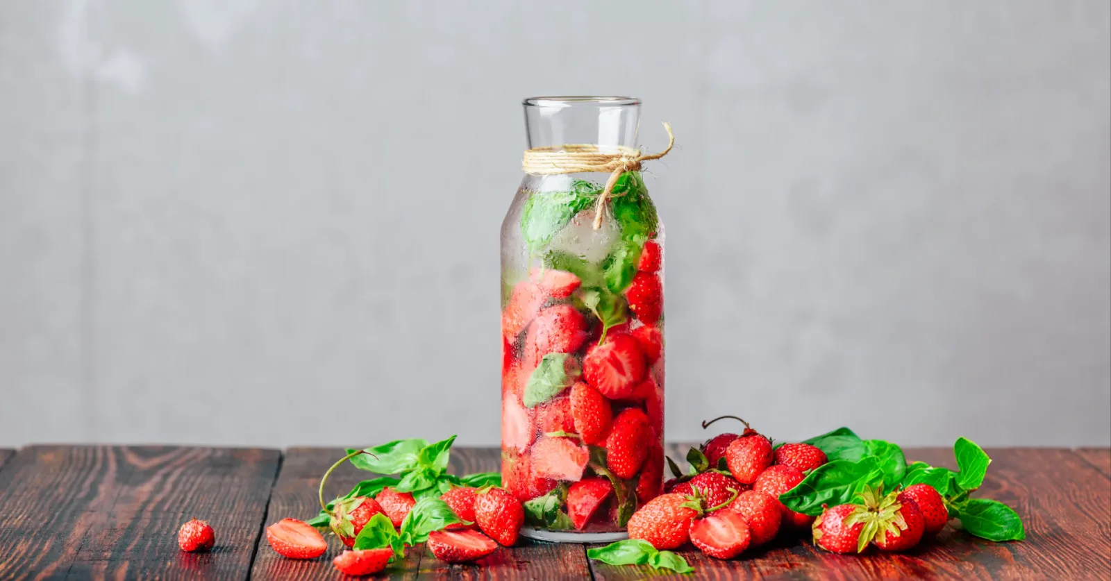 Strawberry basil agua fresca in a glass pitcher with fresh strawberries and basil leaves on a wooden table.